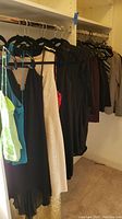 Various women's dresses, jackets, and tops hanging on rack, including black, cream, and gray garments