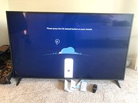 Front view of TV powered on showing setup screen and left stand leg on carpet
