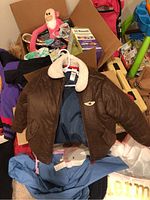 Photo showing brown faux leather jacket with shearling collar laid out flat with various items in background including a pink plush toy and books.