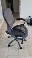 Side view of the black mesh office chair showing curved backrest, padded armrest and wheel base.