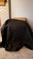 Single black quilted packing blanket displayed over an object against a white wall and beige carpet.