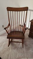 Full front view of the antique wooden rocking chair showing smooth finish, curved arms, and spindled backrest.