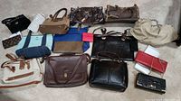 Overview of multiple purses and wallets arranged on carpeted floor showing variety in colors, materials, and styles.