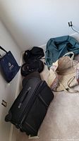 Photo of all bags in corner, showing Tumi roller bag, Eastpak backpack, Pierre Deux floral and beige bags, and other black bags.