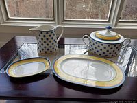 Four items on table: covered tureen, pitcher, large and small platters with yellow band and blue dots.