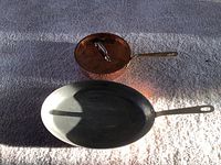 Top view: small copper saucepan with lid and oval copper pan side by side on carpet
