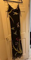 Black gown with floral and butterfly motifs on black background hanging on door