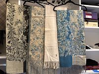 Four scarves hanging on hangers inside a closet, showing varied floral patterns and colors including beige, black, blue and cream