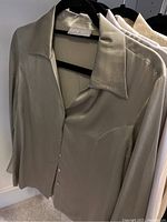 Close-up of beige silk blouse showing smooth fabric, buttons, and collar on a hanger labeled Kate Hill