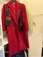 Red long coat displayed on hanger with patterned scarf, showing front buttons and collar detail