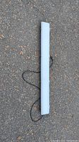 Photo of a 4-foot long, slim LED shop light with a white frosted cover, black power cord attached, resting on pavement.