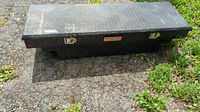 Closed view of black aluminum DeeZee truck tool box showing diamond plate pattern on lid and two locking latches.