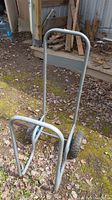 Firewood cart with metal frame, two large wheels, and handles, shown outdoors near stored firewood.