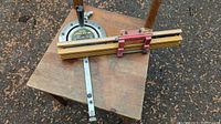 Full view of miter gauge laid on wooden surface showing protractor head, aluminum fence, red carriage and locking knob