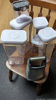All five containers and KitchenAid box grater arranged on a wooden chair showing size and shape
