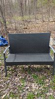 Front view of black synthetic wicker patio loveseat with metal frame outdoors on leaf-covered ground