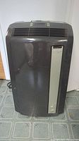 Front view of dark grey DeLonghi portable air conditioner showing grille and side panel