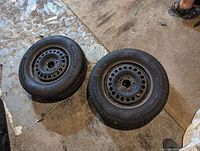 Two black steel rims with new General brand tires lying flat on a barn floor. The tires have visible tread and white sidewall lettering.