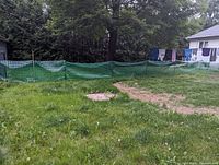 Green plastic snow fence with supporting green poles set up around a yard patch with grass and dirt.