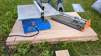 Photo showing both the diamond wheel saw and the manual tile cutter on wooden boards outdoors.