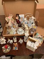 Photo of angel figurines including ceramic angel lamp, resin and porcelain angels, and some boxed items on and inside a cardboard box.