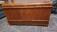 Front view of cedar chest showing curved top and decorative lower edge with visible marks and scratches.