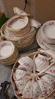 Photo of china cups and saucers with floral pink rose patterns, some pieces padded in sleeve for protection.