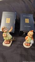 Two Hummel figurines displayed side by side with their original navy blue Exclusive Edition boxes behind them.