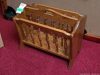 Front angled view showing spindle sides and overall structure of the oak magazine rack on red carpet.