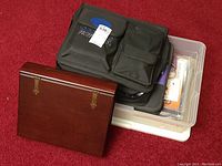 Wooden keepsake box closed next to plastic bins and fabric carry cases on a red carpet.