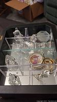 View of wall mount display box divided into sections holding crystal figurines and miniature plates, showing condition and layout of items