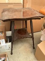 Front view of vintage wooden occasional table showing scalloped top, turned legs, and lower shelf with visible wear and finish damage.