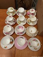Overview of all 12 tea cups and saucers arranged on wooden surface