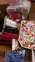 View of four small wallets, floral scarf, a small white box, two manicure kits with red star-patterned cases, and other wrapped items.