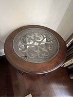 Top-down view of round glass inset showing ornate wrought iron scrollwork and surrounding wood frame.