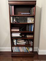 Full view of dark wooden bookcase against wall with books on shelves.