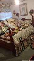 Overview of antique wood bed with floral bedding, piled textiles and books on mattress.