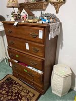Front view of a tall wooden chest of drawers with brass handles and some decorative items on top.