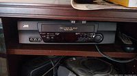 Front view of JVC video cassette recorder showing the model and control buttons with remote control.