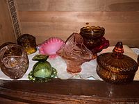 Full view of the glass baskets, lidded bowl, and candy dishes in amber, pink, and green colors arranged on a wooden surface.
