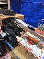 Black electric guitar resting on a Sony VCR and Smirnoff box