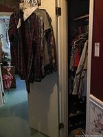 Photo of multiple men's shirts and jackets hanging on hangers in doorway, including a plaid shirt and solid colored shirts.