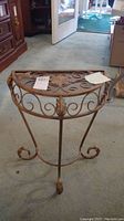 Front view of the metal half-moon table showing the scrollwork and floral detail on top and curled feet on legs.
