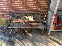 Front view of outdoor bench showing decorative floral metal backrest and wood slat seat in weathered condition.