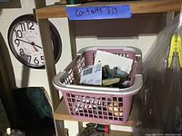 Pink plastic basket filled with various small items, including sewing supplies, placed on a wooden shelf