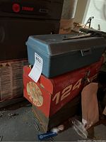 Green plastic toolbox sitting on top of a red metal Castrol GTX 124 toolbox with a third metal toolbox underneath. Dust and dirt visible around boxes.