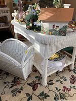 Photo showing white wicker coffee table with lower shelf and matching white wicker magazine basket beside it, partially filled with papers and items on table top