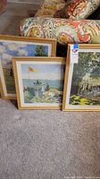 Three framed Claude Monet prints positioned leaned on carpet near colorful couch, showing details of print artwork and frames.