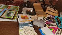 Overview of various art supplies including paint trays, sketchbooks, art containers, and framed artwork spread on a surface