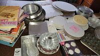 Wide shot of baking supplies and cookbooks showing various baking pans, cake stands, and part of the cookbook stack